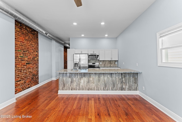 kitchen featuring light stone counters, brick wall, tasteful backsplash, white cabinetry, and appliances with stainless steel finishes