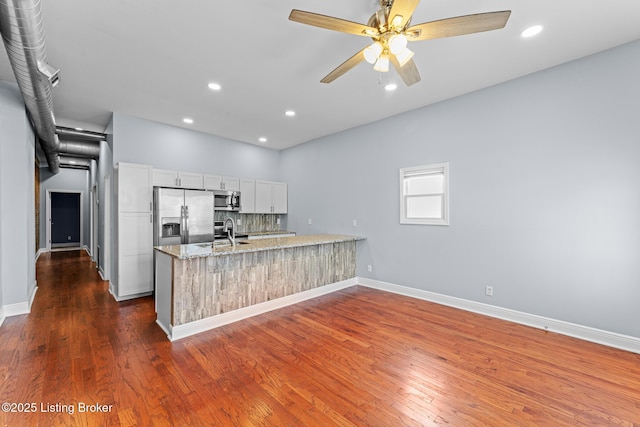 kitchen with stainless steel appliances, light stone countertops, white cabinets, backsplash, and sink