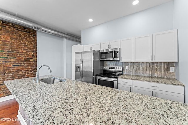 kitchen featuring stainless steel appliances, sink, white cabinetry, backsplash, and brick wall