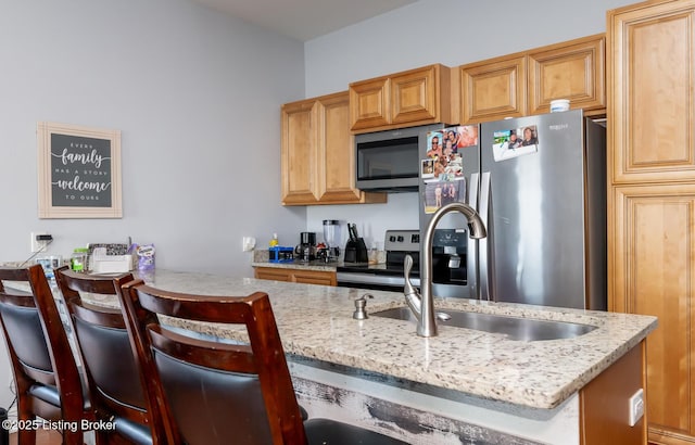 kitchen with stainless steel appliances, a kitchen bar, sink, and light stone countertops