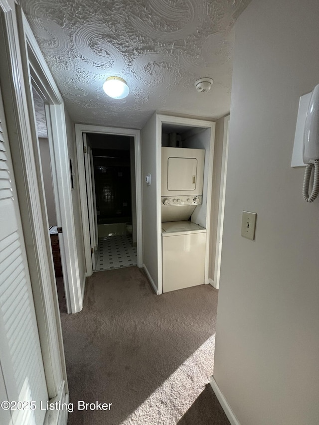 hallway featuring carpet, stacked washer and clothes dryer, and a textured ceiling