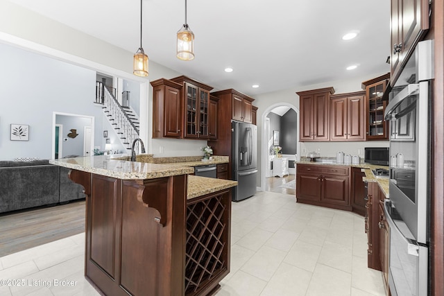 kitchen with a breakfast bar, dark brown cabinetry, hanging light fixtures, light stone countertops, and stainless steel appliances