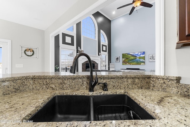 kitchen with ceiling fan, crown molding, sink, and light stone counters