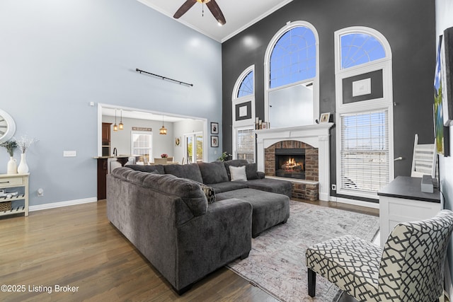 living room featuring a brick fireplace, crown molding, a towering ceiling, and dark hardwood / wood-style floors