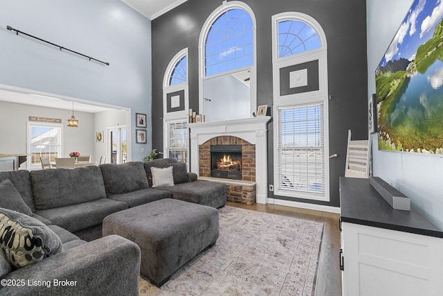 living room with a brick fireplace, a high ceiling, ornamental molding, and hardwood / wood-style flooring