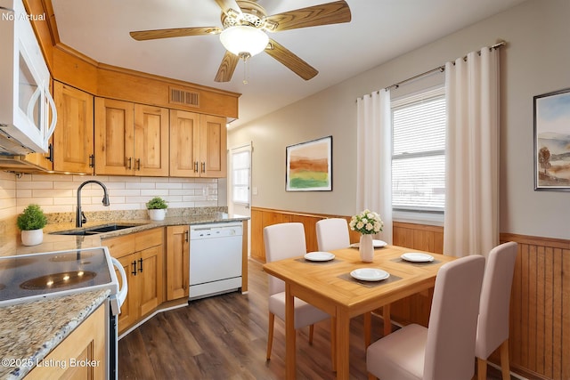 kitchen with dark hardwood / wood-style floors, wood walls, sink, light stone countertops, and white appliances