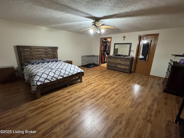 bedroom with ceiling fan, wood-type flooring, a textured ceiling, a walk in closet, and a closet