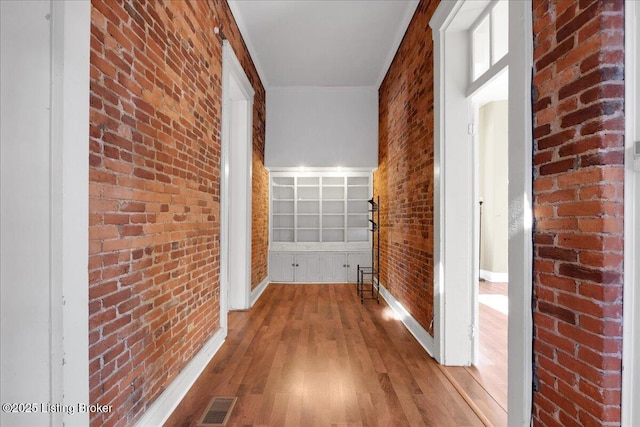 hall with wood-type flooring and brick wall