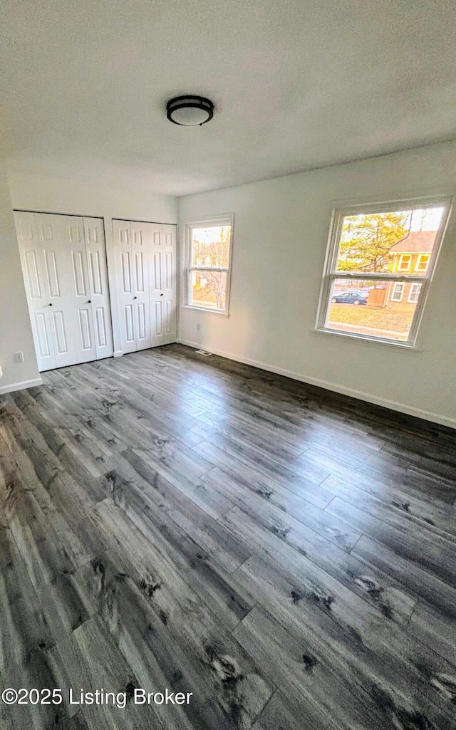 unfurnished bedroom featuring a textured ceiling, two closets, and dark hardwood / wood-style floors