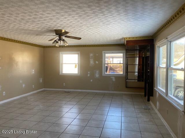 empty room with ceiling fan, light tile patterned flooring, ornamental molding, and a healthy amount of sunlight