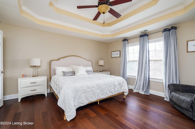 bedroom featuring dark wood-type flooring, ceiling fan, ornamental molding, and a tray ceiling