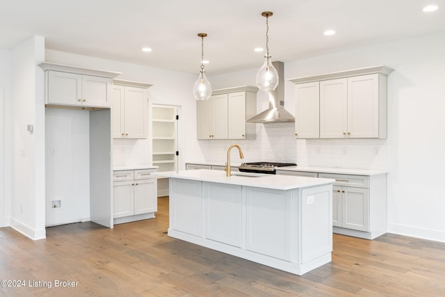 kitchen with decorative light fixtures, light hardwood / wood-style floors, white cabinetry, and a center island with sink