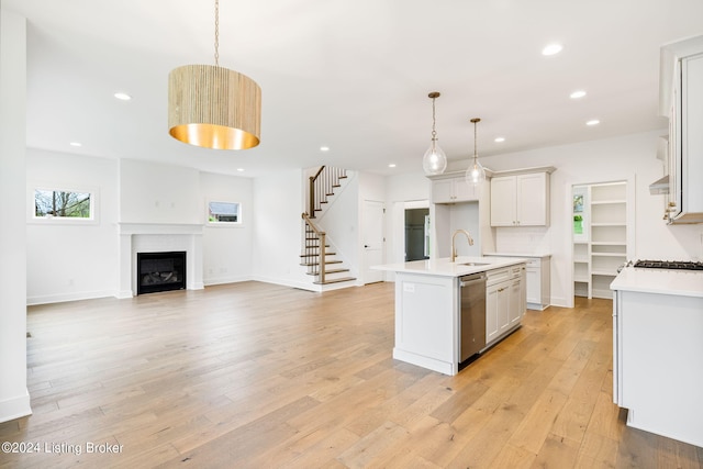 kitchen with white cabinets, decorative backsplash, hanging light fixtures, stainless steel dishwasher, and a center island with sink