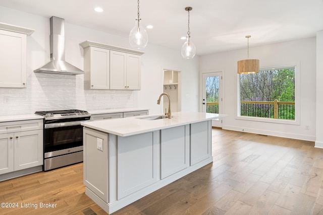 kitchen featuring stainless steel gas stove, sink, hanging light fixtures, and wall chimney exhaust hood