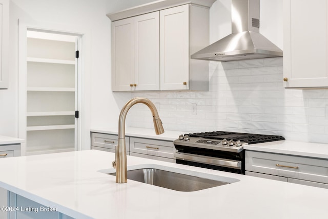 kitchen featuring stainless steel gas range, sink, backsplash, and wall chimney range hood