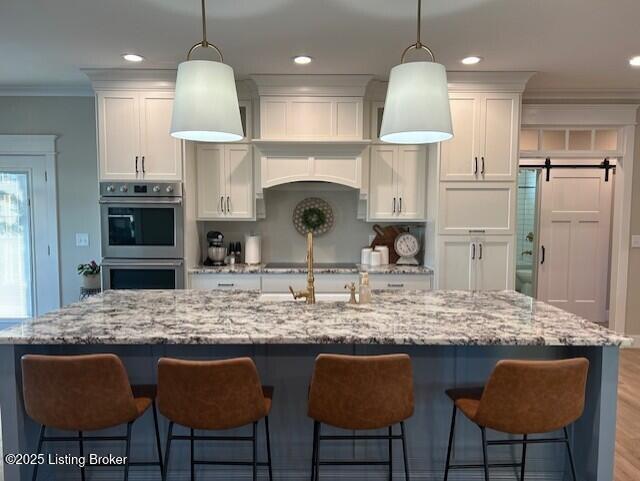 kitchen with hanging light fixtures, double oven, a large island with sink, and white cabinetry