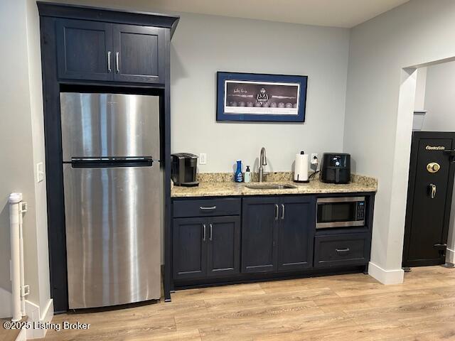 bar featuring light hardwood / wood-style floors, sink, stainless steel appliances, and light stone countertops