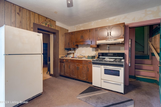 kitchen featuring sink, white appliances, a textured ceiling, and wooden walls