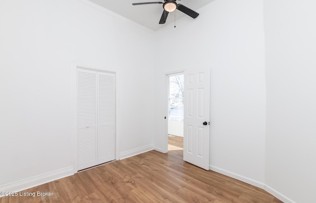 unfurnished bedroom with ceiling fan, a closet, a towering ceiling, and light wood-type flooring