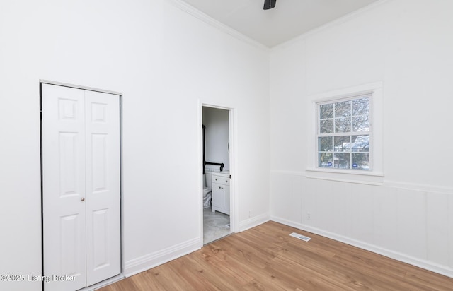 unfurnished bedroom featuring ensuite bathroom, wood-type flooring, a closet, ornamental molding, and ceiling fan