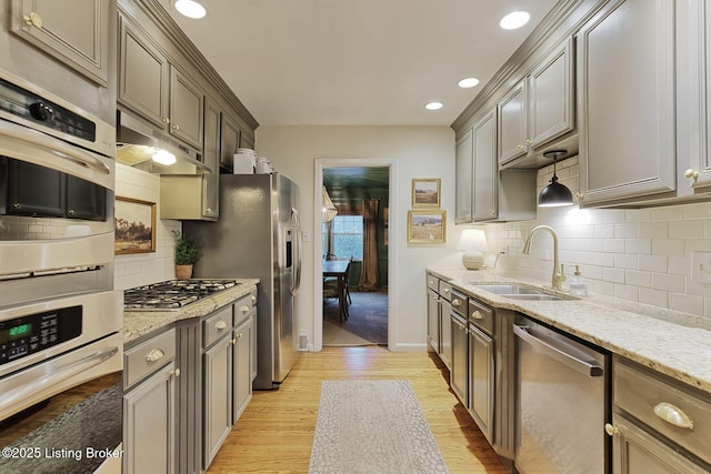 kitchen featuring backsplash, light hardwood / wood-style floors, sink, light stone countertops, and stainless steel appliances