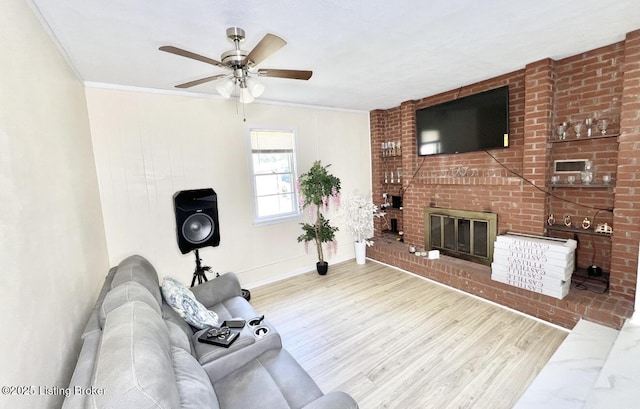 living room with light hardwood / wood-style floors, crown molding, ceiling fan, and a fireplace