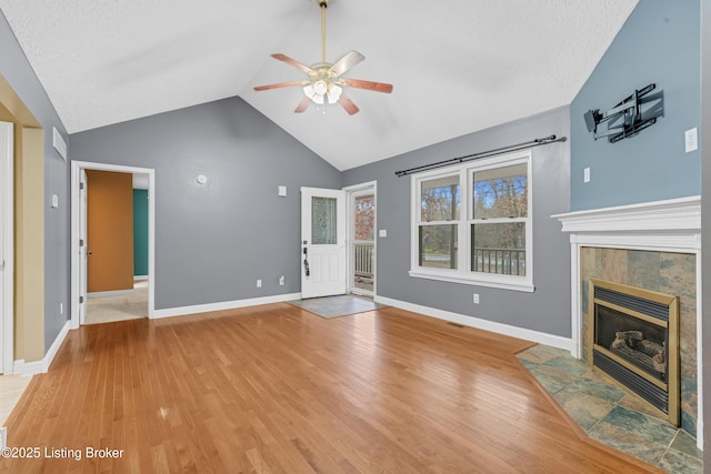 unfurnished living room featuring ceiling fan, vaulted ceiling, a tile fireplace, hardwood / wood-style flooring, and a textured ceiling