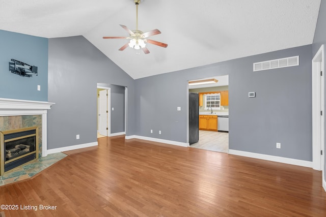 unfurnished living room with ceiling fan, light wood-type flooring, lofted ceiling, a tile fireplace, and sink