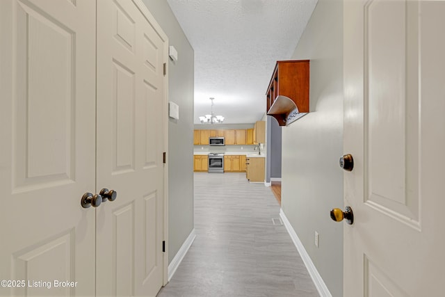 hall featuring sink, an inviting chandelier, a textured ceiling, and light hardwood / wood-style floors