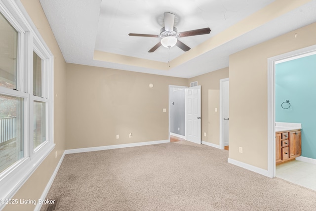 unfurnished bedroom featuring ceiling fan, light colored carpet, connected bathroom, and a raised ceiling