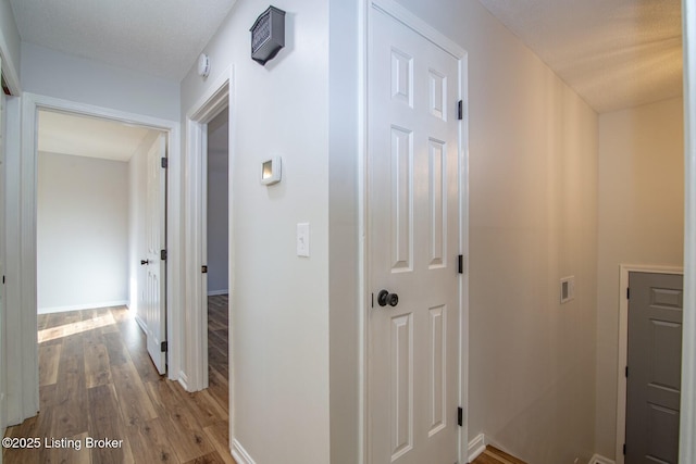 corridor with a textured ceiling and light hardwood / wood-style flooring