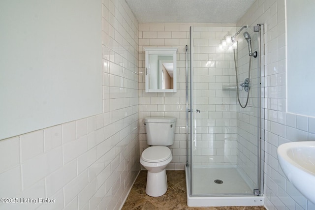 bathroom with toilet, a shower with shower door, tile walls, a textured ceiling, and sink