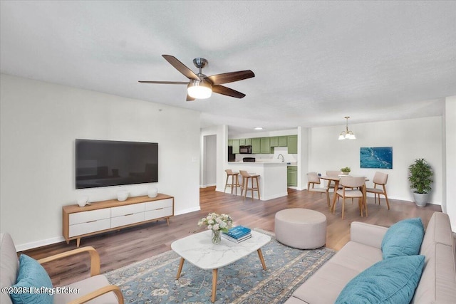 living room featuring sink, ceiling fan with notable chandelier, a textured ceiling, and hardwood / wood-style flooring