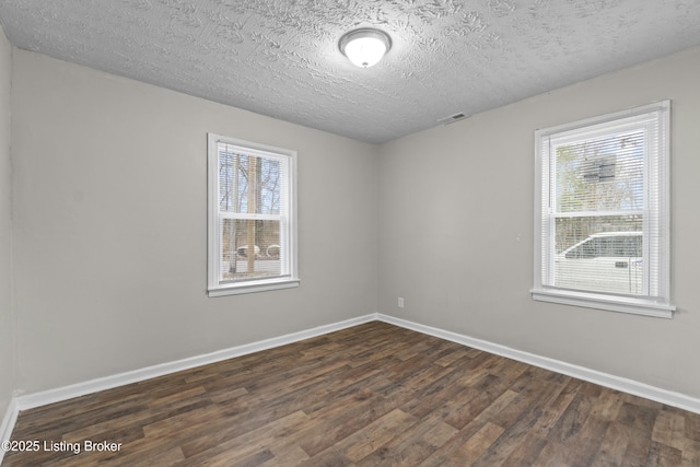 spare room featuring dark wood finished floors, visible vents, a textured ceiling, and baseboards