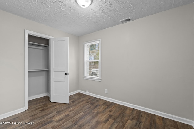 unfurnished bedroom featuring visible vents, a textured ceiling, dark wood-style floors, a closet, and baseboards