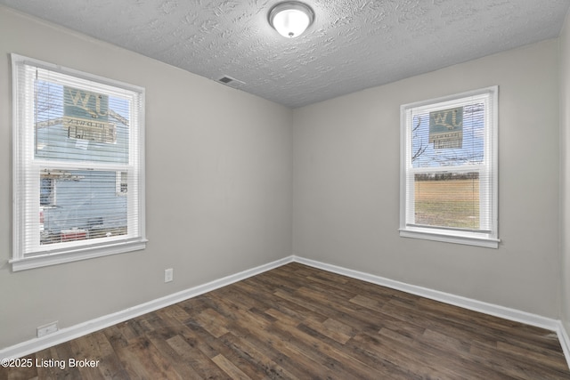 unfurnished room with dark wood finished floors, baseboards, visible vents, and a wealth of natural light