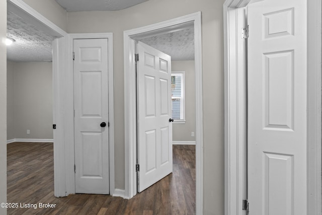 corridor with a textured ceiling, baseboards, and dark wood-style flooring