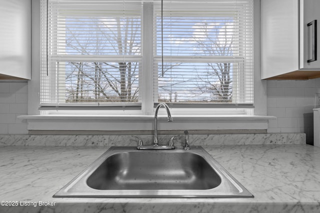 kitchen featuring light stone countertops, white cabinetry, and a sink