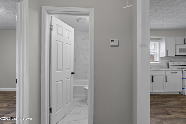 corridor with baseboards, marble finish floor, and a textured ceiling