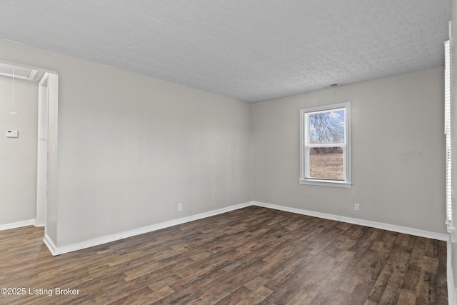 empty room featuring dark wood finished floors, visible vents, attic access, and baseboards