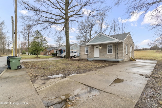 bungalow with a porch, stone siding, and a shingled roof