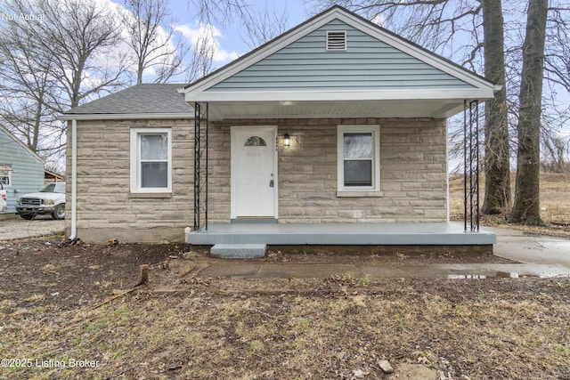 view of front facade featuring stone siding, covered porch, and roof with shingles