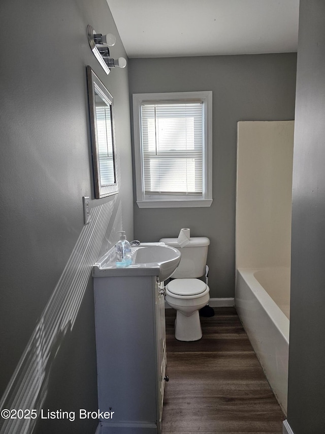 bathroom with hardwood / wood-style flooring, toilet, a bath, and vanity