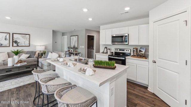 kitchen with white cabinets, stainless steel appliances, a breakfast bar area, and a kitchen island with sink