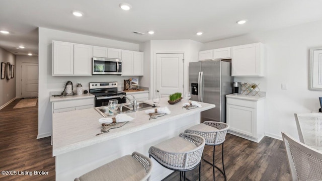 kitchen with white cabinetry, stainless steel appliances, a kitchen island with sink, dark wood-type flooring, and a breakfast bar