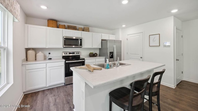 kitchen with appliances with stainless steel finishes, a kitchen bar, white cabinetry, an island with sink, and sink