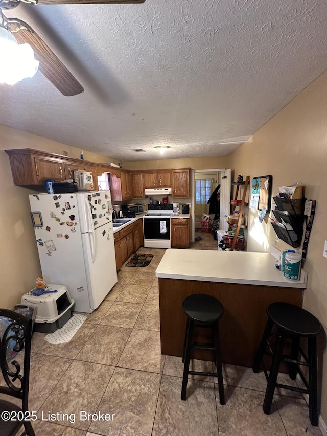 kitchen with white fridge, kitchen peninsula, ceiling fan, electric stove, and a breakfast bar