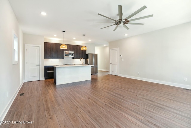 kitchen featuring dark brown cabinetry, open floor plan, stainless steel appliances, and wood finished floors