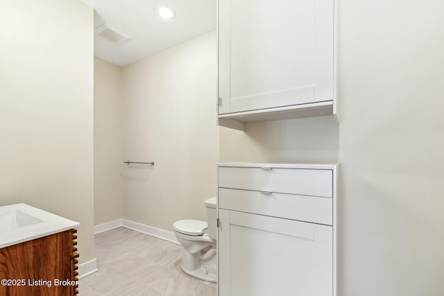 half bath featuring vanity, toilet, baseboards, and visible vents