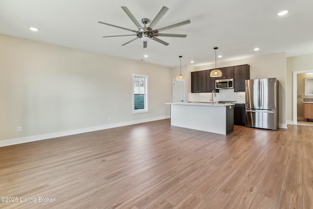 kitchen featuring open floor plan, stainless steel appliances, light wood finished floors, dark brown cabinets, and light countertops